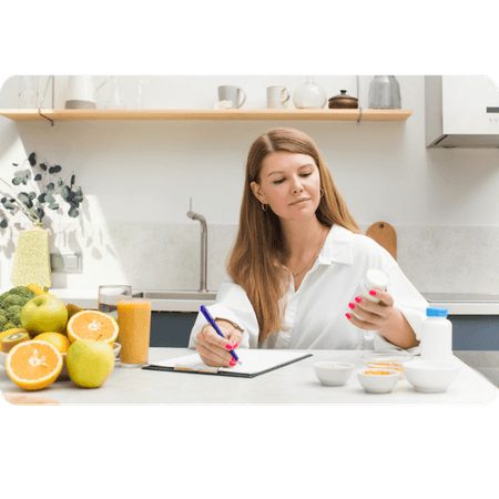A lady at a desk examining a tub of tablets surrounded by fruit