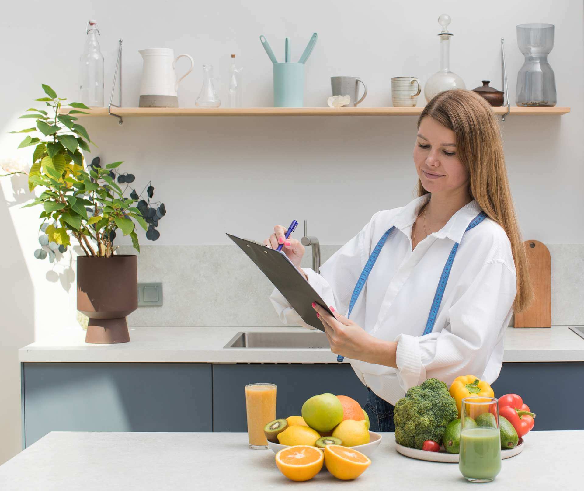 A lady with a clipboard in a kitchen. She's surrounded by healthy food.