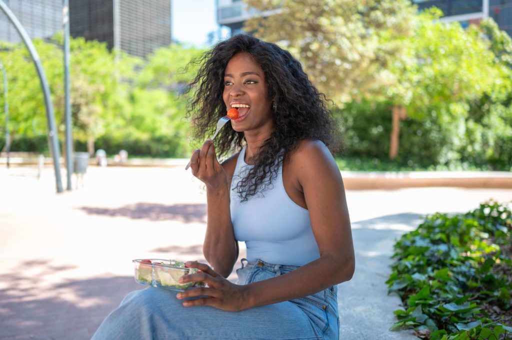 A lady sitting outside in a park eating a healthy salad