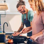 A man and a woman at a sink preparing food together