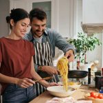 A man and a woman in a kitchen preparing a meal of spaghetti