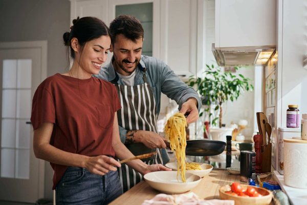 A man and a woman in a kitchen preparing a meal of spaghetti