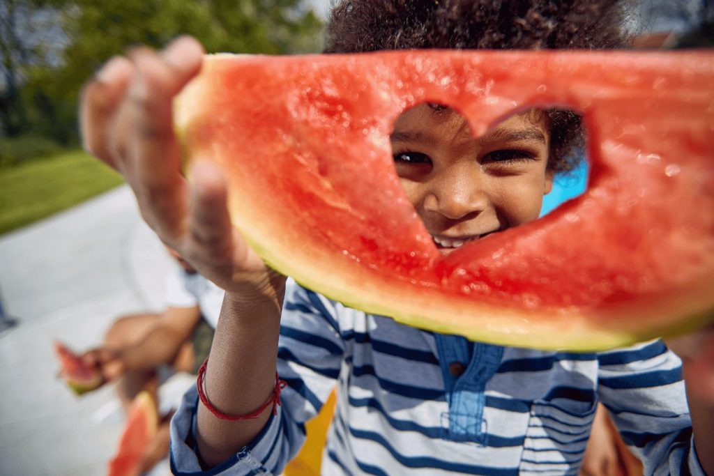 Child holding up watermelon with a heart shape cut out of it.