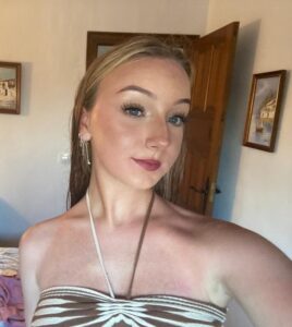 young woman wearing make up and a summer top while posing for a selfie in a room.