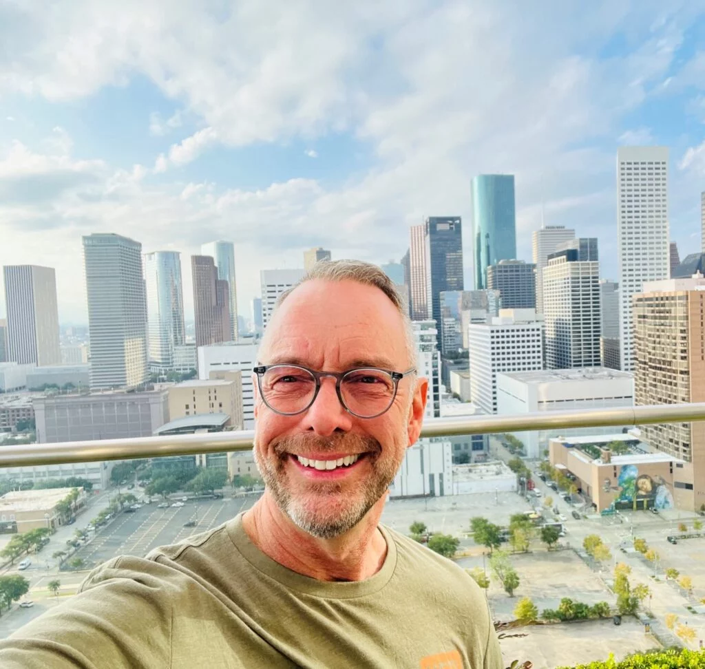 man in a green shirt taking a selfie against a city landscape