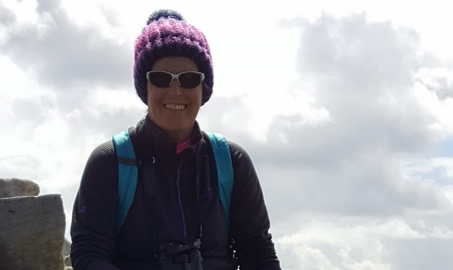 woman wearing hiking gear, posing for the camera with a natural landscape in the background