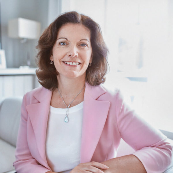 middle aged woman in a pink jacket sitting on a sofa and smiling at the camera