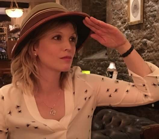 young woman wearing a brown hat and a white top in a restaurant doing a salute