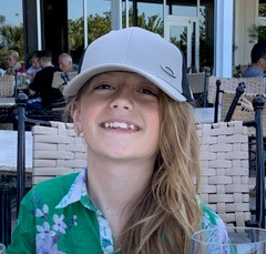 young girl with a light grey cap and a flowery green shirt smiling at the camera