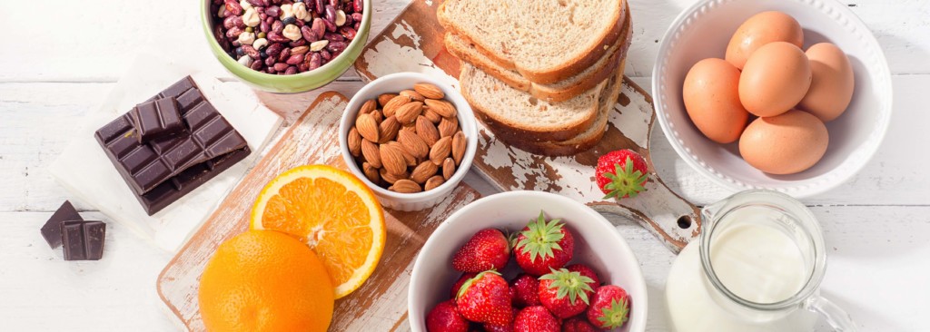 Food on display on a white table (including bread, eggs, milk, nuts, strawberries, oranges, chocolate)