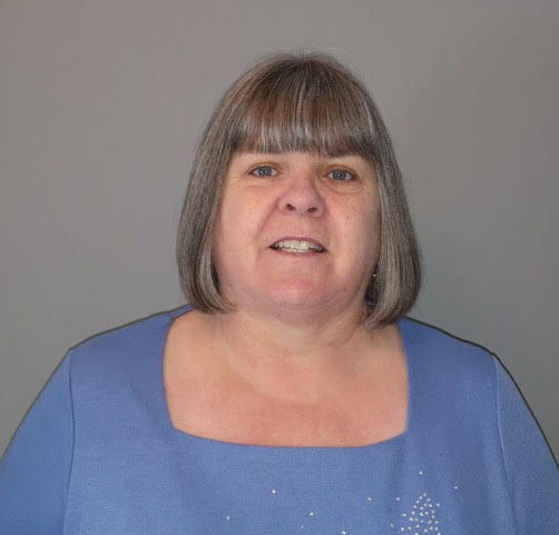 a woman in a blue top posing for a picture against a grey background