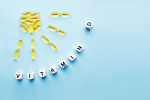Vitamin D Yellow capsules in the form of the sun with rays and the word vitamin D from white cubes with letters on a blue background. VITAMIN D word for healthy and medical concept. Sunshine vitamin health benefits