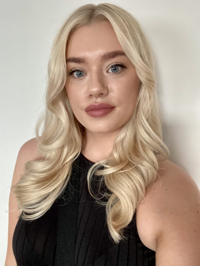 A young woman with long blonde hair and a black top doing a selfie