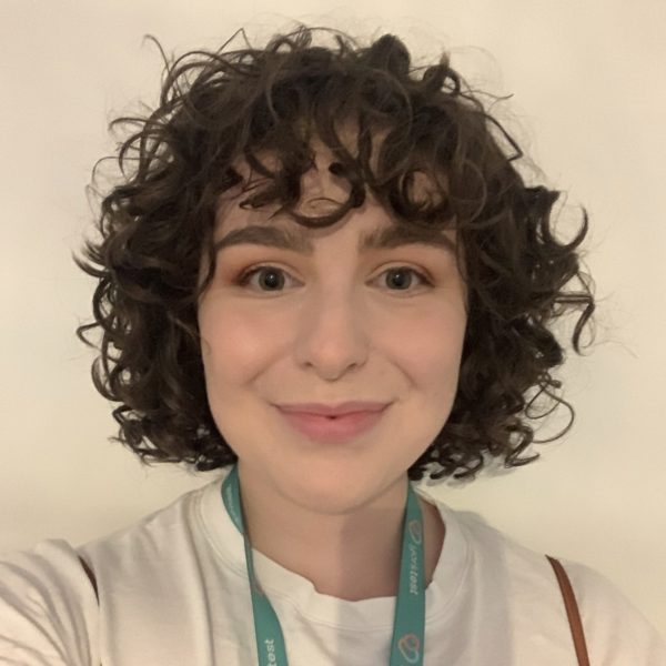 Young girl with short curly black hair smiling at the camera and wearing a YorkTest lanyard resting on her white t-shirt.