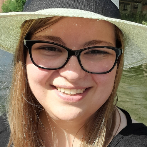 A young girl with glasses and a white hat smiling.