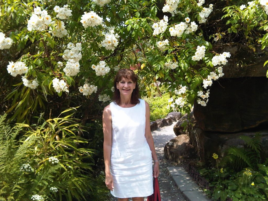 Patty Haynes, a female YorkTest customer, posing for the camera in a white dress with a tree in bloom in the background.