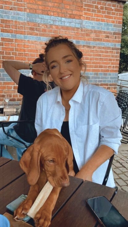 young woman in a white shirt posing for the camera with a young brown dog