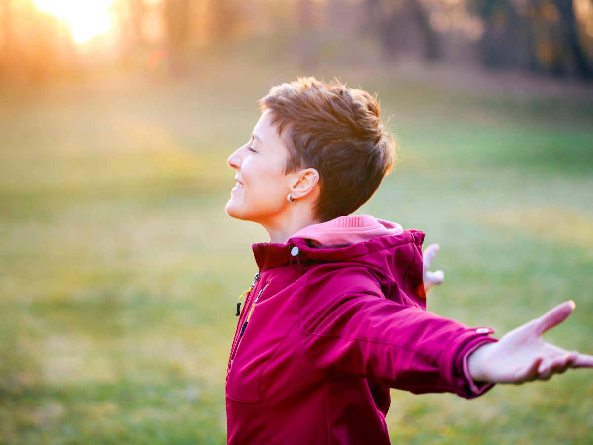 Woman wearing a red jacket stands with her arms wide enjoying the sun