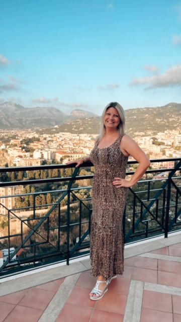 Debbs Hill, a YorkTest customer who took a Premium Food Intolerance Test to identify her trigger food and is smiling happily from a balcony overlooking a sun lit city.