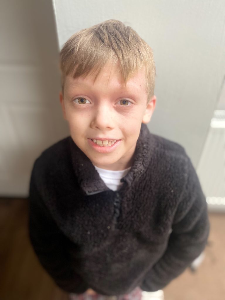 little boy with blond hair and a black sweater looking up and smiling at the camera