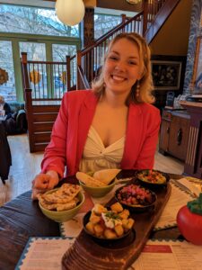 young woman in a red jacket, smiling at the camera while sitting down in a restaurant