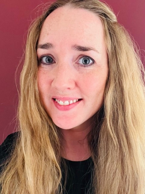 Blonde woman with long hair smiling at the camera against a red background