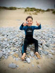 small boy smiling while sat on a rocky beach