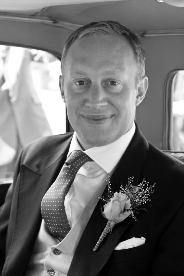 white and black picture of a middle aged man in a car wearing a smart suit.