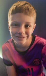 9 year old boy with light hair and a red t-shirt smiling at the camera