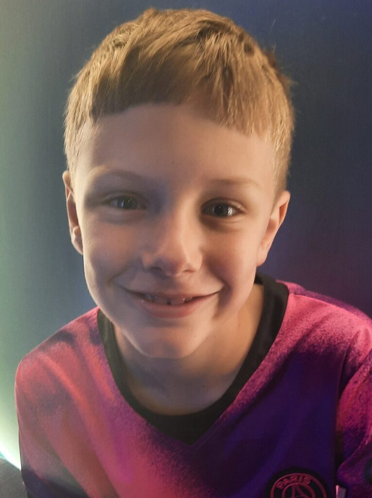 9 year old boy with light hair and a red t-shirt smiling at the camera
