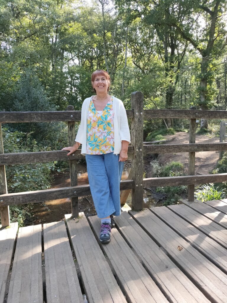 Middle aged woman in jeans posing for a photo in the park on a bridge