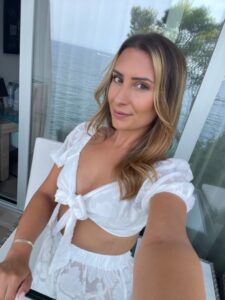 young woman dressed in a white two piece summer outfit and smiling at the camera