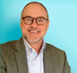 middle aged man in a suit smiling at the camera against a teal background