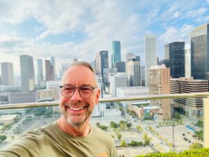 man in a green shirt taking a selfie against a city landscape