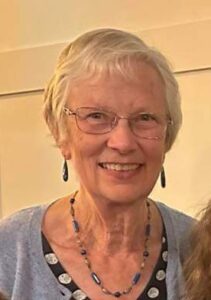 older woman wearing a teal necklace and earrings smiling at the camera