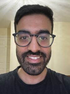 man in his 30s wearing glasses and smiling at the camera